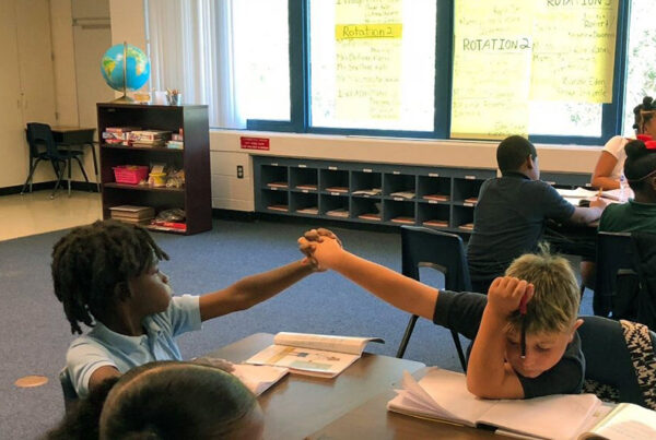 Two elementary-age students exchange a high-five as they work together in a calm, focused, and positive manner, leading and managing their own academic tasks and behavior.