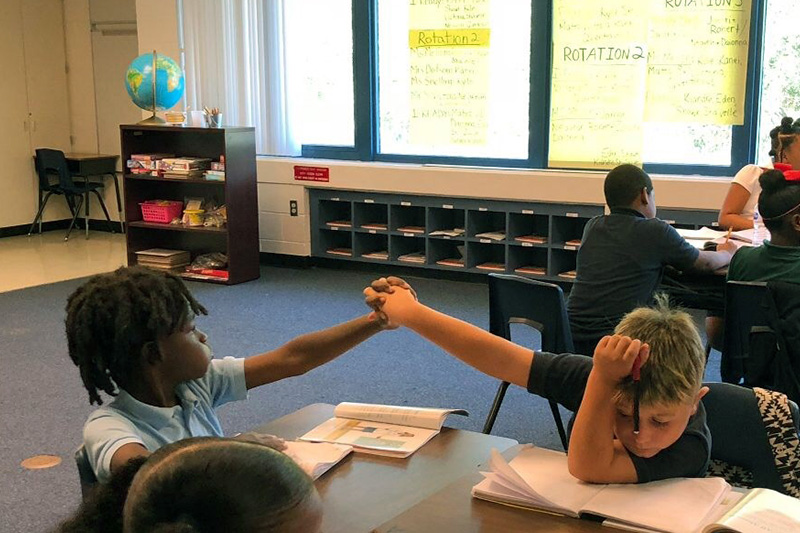 Two elementary-age students exchange a high-five as they work together in a calm, focused, and positive manner, leading and managing their own academic tasks and behavior.