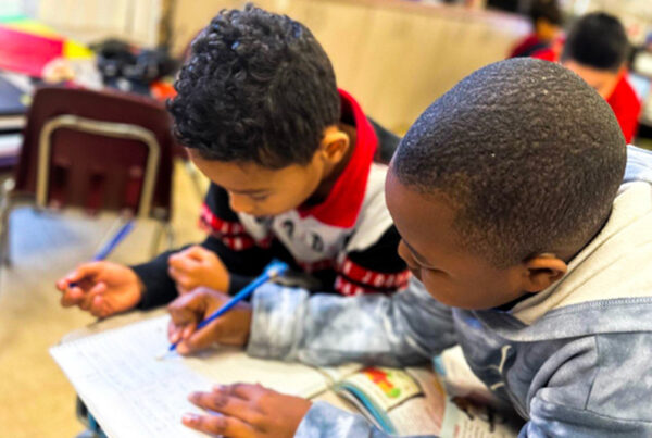 Elementary-age students sit around a table together, deep in discussion and using student-driven engagement strategies like team roles and academically rigorous tasks, which are important in raising achievement and closing gaps.