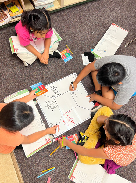 Four elementary-age students sit on the floor together, engaged in a team task and building the important skills of persistence as they work through a math problem together. 