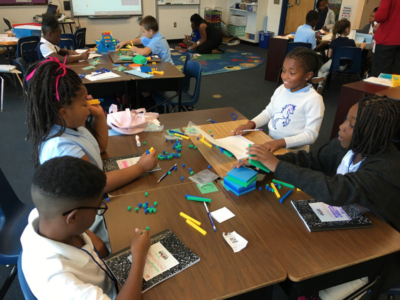 Four students from Lakewood Elementary sit together in a team, working together with notebooks and math manipulatives on a rigorous task.