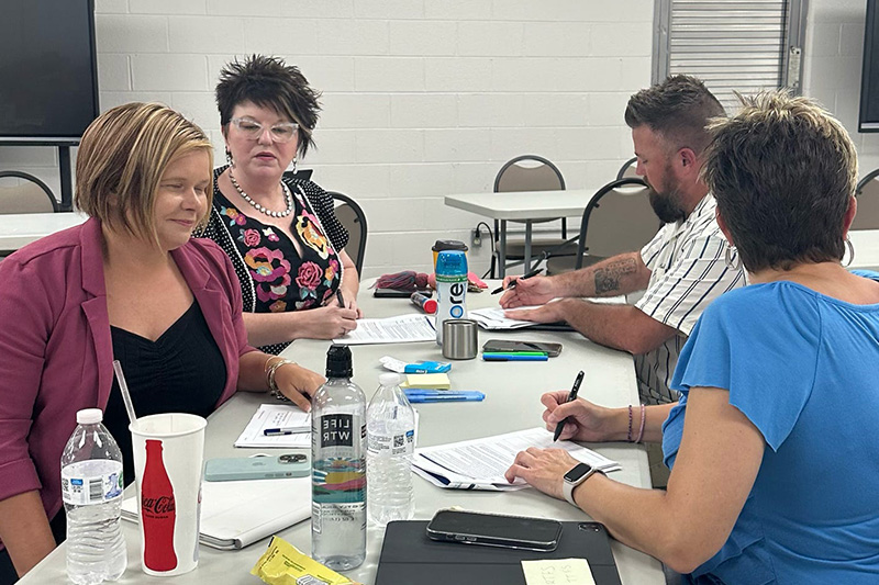 Principals and other school leaders and administrators sit together at a table, discussing and writing on papers as they learn about the Model of Instruction for Deeper Learning, including how to increase teacher agency.