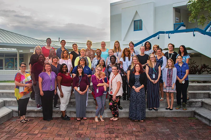 About 30 teachers, leaders, and school staff from Lakewood Elementary stand on the steps in front of their school, smiling proudly at their improvements and achievements as they overcame teacher turnover and saw less teachers leaving the profession.