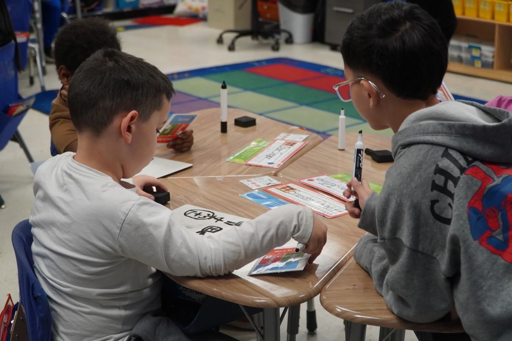 Three elementary students sit at a table together focusing on their work and using colorful tools from the Model of Instruction for Deeper Learning. More parents and families are seeking experiences like these and often choose microschools that offer a small, highly personalized learning experience.