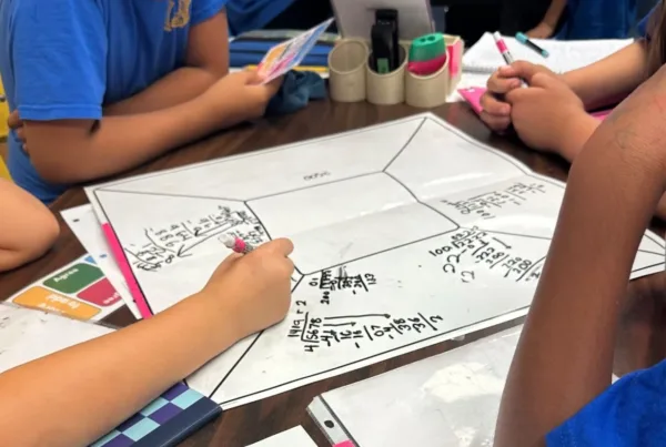 Four elementary age students sit together at a table working on math problems collaboratively as they experience the high-rigor, team-based learning that raises achievement after their school adopted RigorWalk.