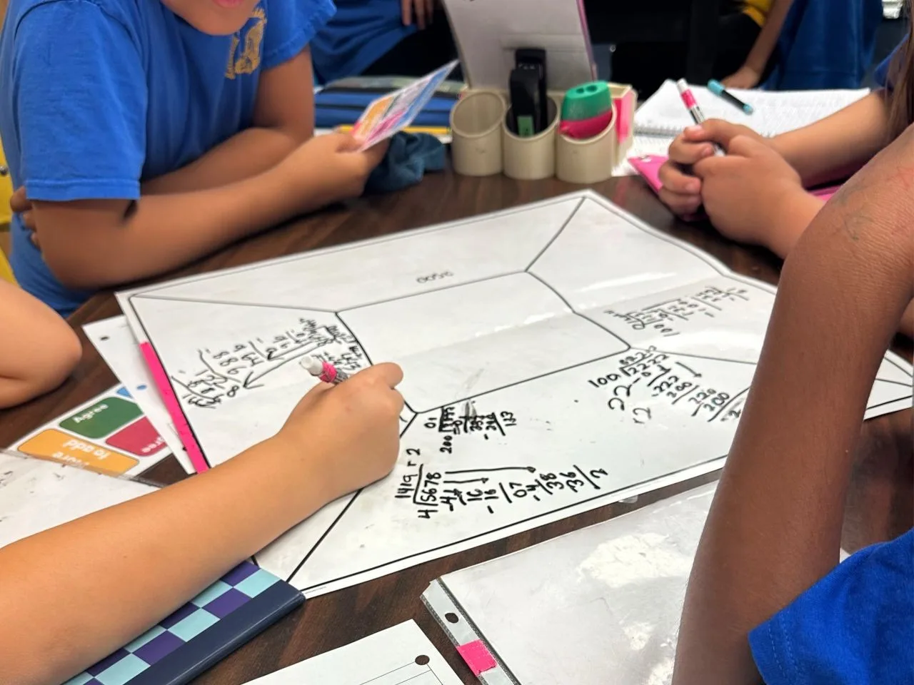 Four elementary age students sit together at a table working on math problems collaboratively as they experience the high-rigor, team-based learning that raises achievement after their school adopted RigorWalk.