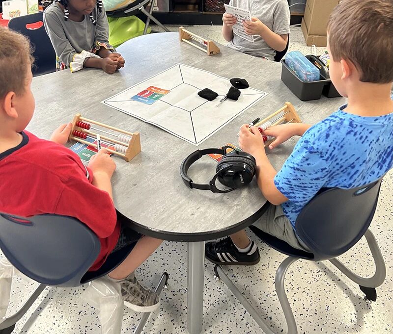 Four students sit at a table, working together with math tools and resources from the Model of Instruction for Deeper Learning, which was implemented districtwide at Cedar Rapids Community School District.