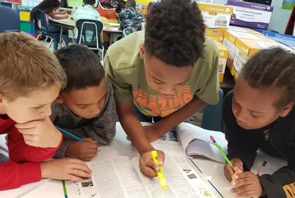 Four students from Moseley Elementary, featured in a turnaround school case study, lean over a table together with highlighters and pencils as they collaborate in a rigorous team as part of the Model of Instruction for Deeper Learning.