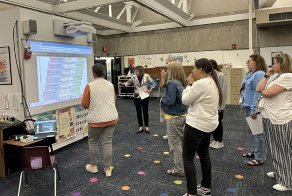 About 8 school leaders standing in a group analyzing comprehensive needs assessment data with the SIMM framework at Nixon Elementary School, Cedar Rapids, Iowa.