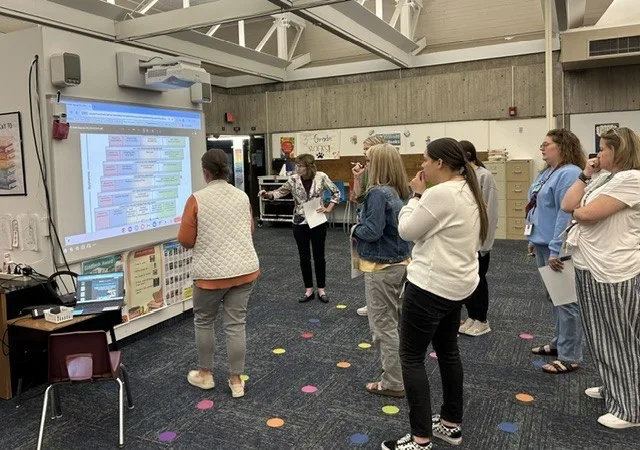 About 8 school leaders standing in a group analyzing comprehensive needs assessment data with the SIMM framework at Nixon Elementary School, Cedar Rapids, Iowa.