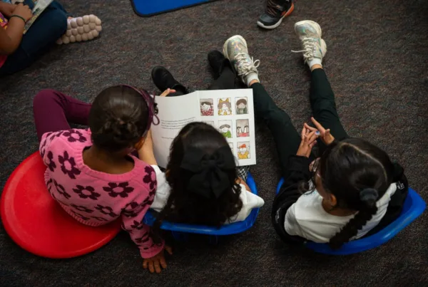 Three elementary students sit on floor cushions reading a picture book together in a Colorado Springs School District 11 classroom, part of a research study on the Model of Instruction for Deeper Learning and its impact on ELA and math achievement gains.