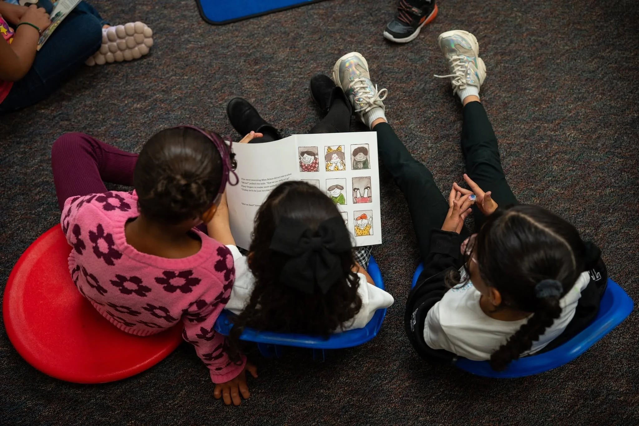 Three elementary students sit on floor cushions reading a picture book together in a Colorado Springs School District 11 classroom, part of a research study on the Model of Instruction for Deeper Learning and its impact on ELA and math achievement gains.