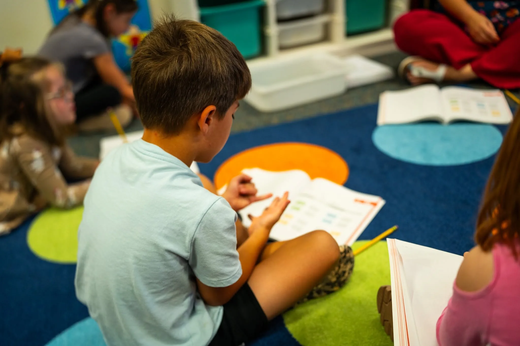 Elementary students sit on a classroom carpet in Colorado Springs School District 11, working from printed high-quality instructional materials during a student-led team lesson.